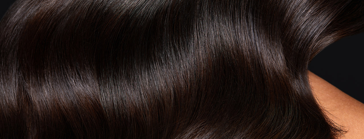 Close up of a woman with hand under shiny black hair.