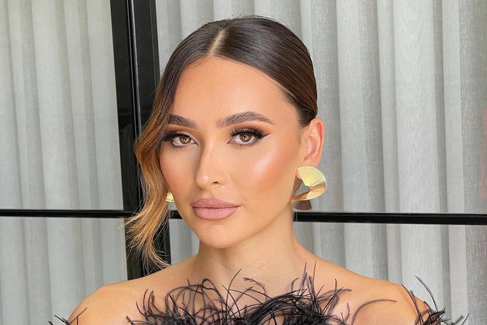 head shot of female model with hair tioed back wearing gold earrings