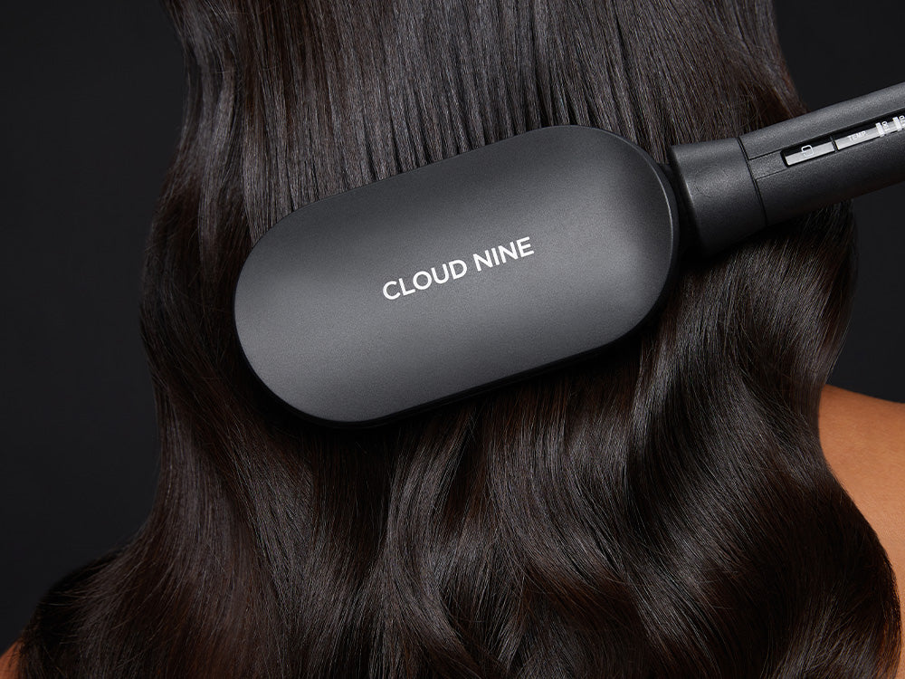 A close up of the CLOUD NINE Hot Brush gliding through wavy black hair.