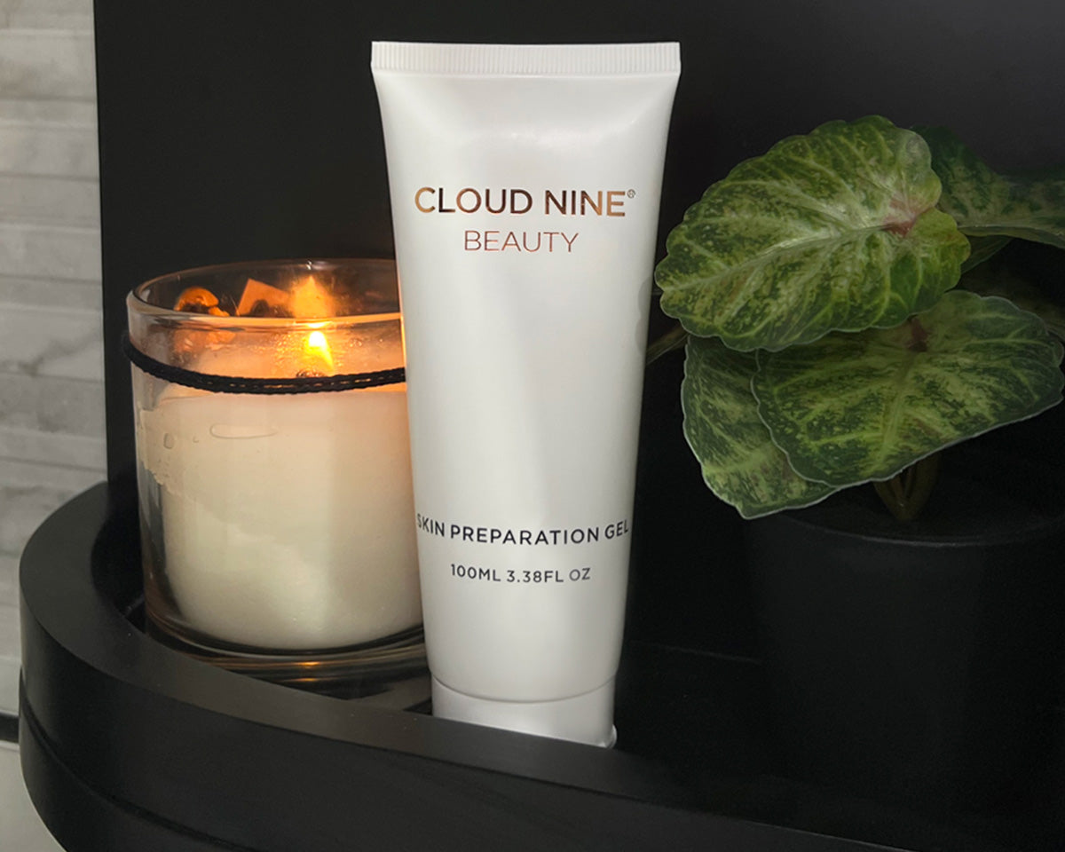 A image of a bottle of CLOUD NINE Beauty Skin Conductive Gel placed on a black shelf next to a lit candle and a plant.