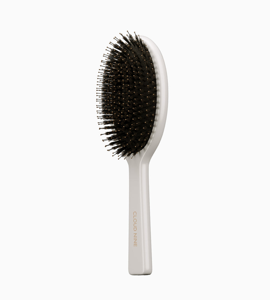 Full view at an angle of a white CLOUD NINE dressing brush with black bristles.