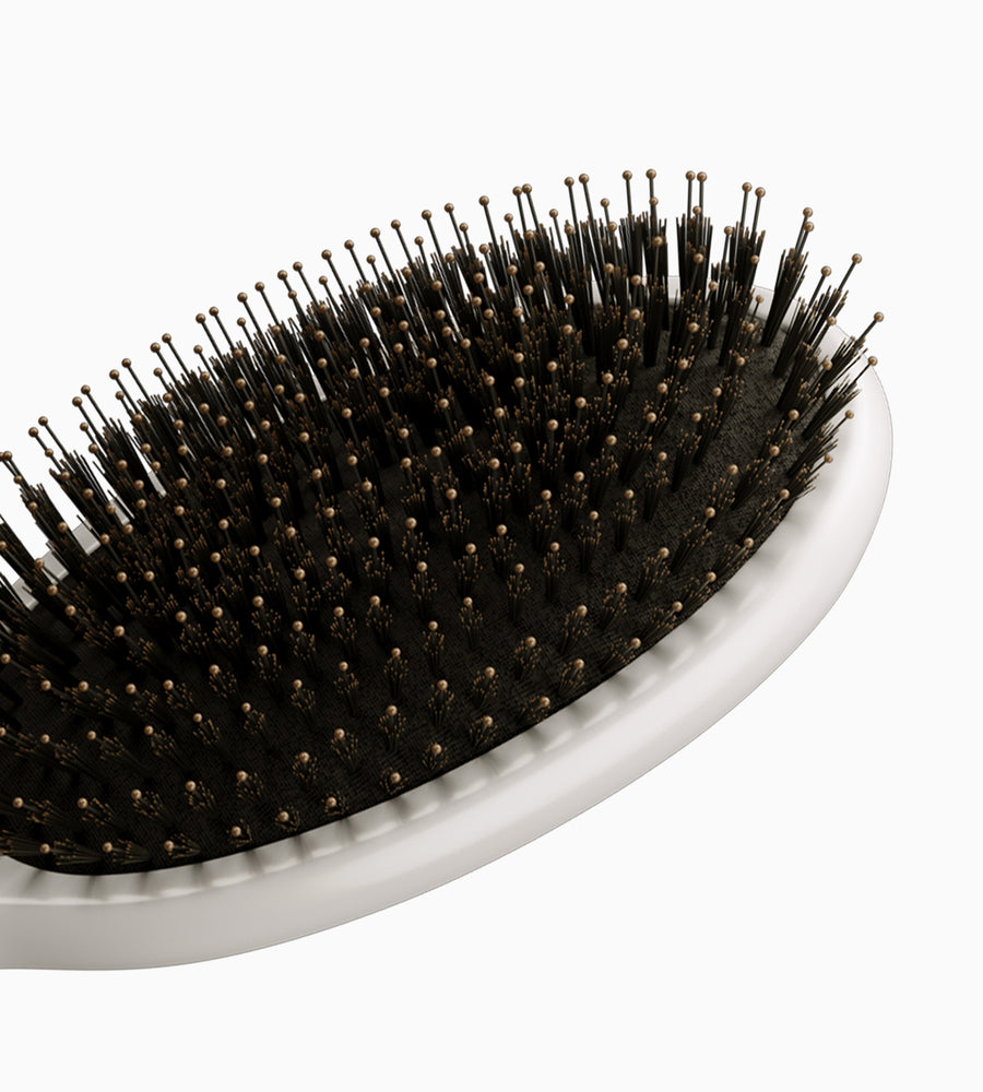 Cropped view of a white dressing brush with black bristles.