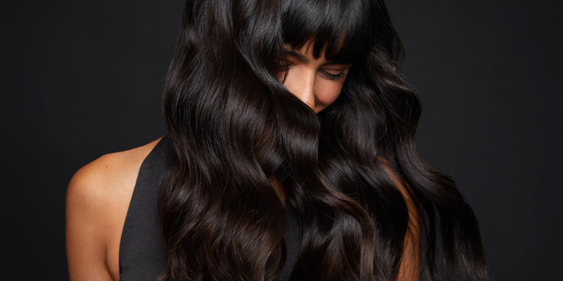 Model with black wavy hair covering most of her face against a black background.