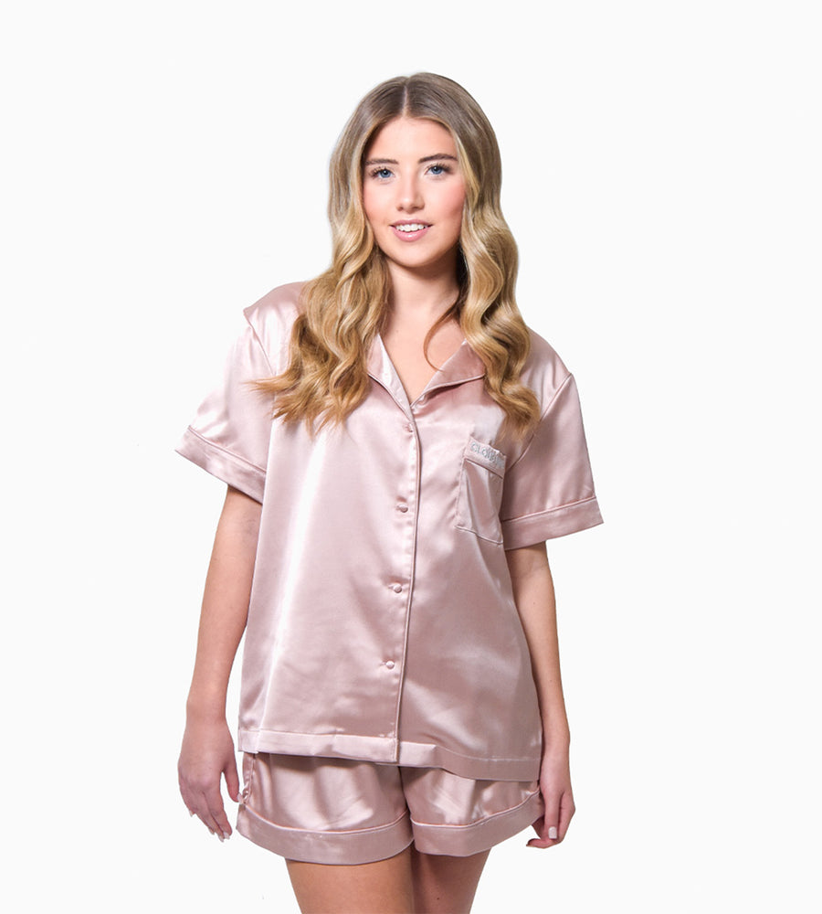 Blonde Model facing forward wearing the pink silk pyjama shorts and short-sleeved shirt against a white background.