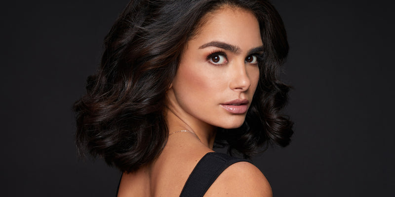 Model with curly short brown hair looking over her shoulder at the camera.