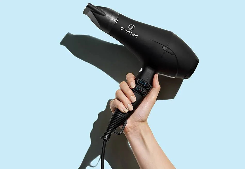 A hand holding The black Airshot with the nozzle attachment on a light blue background.