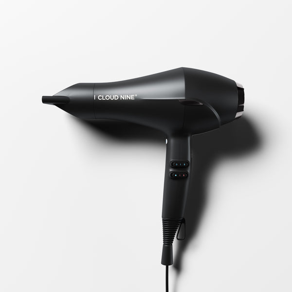 Cloud Nine Airshot hair dryer in Black with nozzle attached, speed and heat switch controls on handle, shown at an angle on a white background