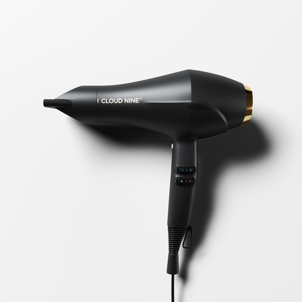 Cloud Nine Airshot hair dryer in Black with Gold filter detail. Shown with nozzle attached, speed and heat switch controls on handle, at an angle on a white background