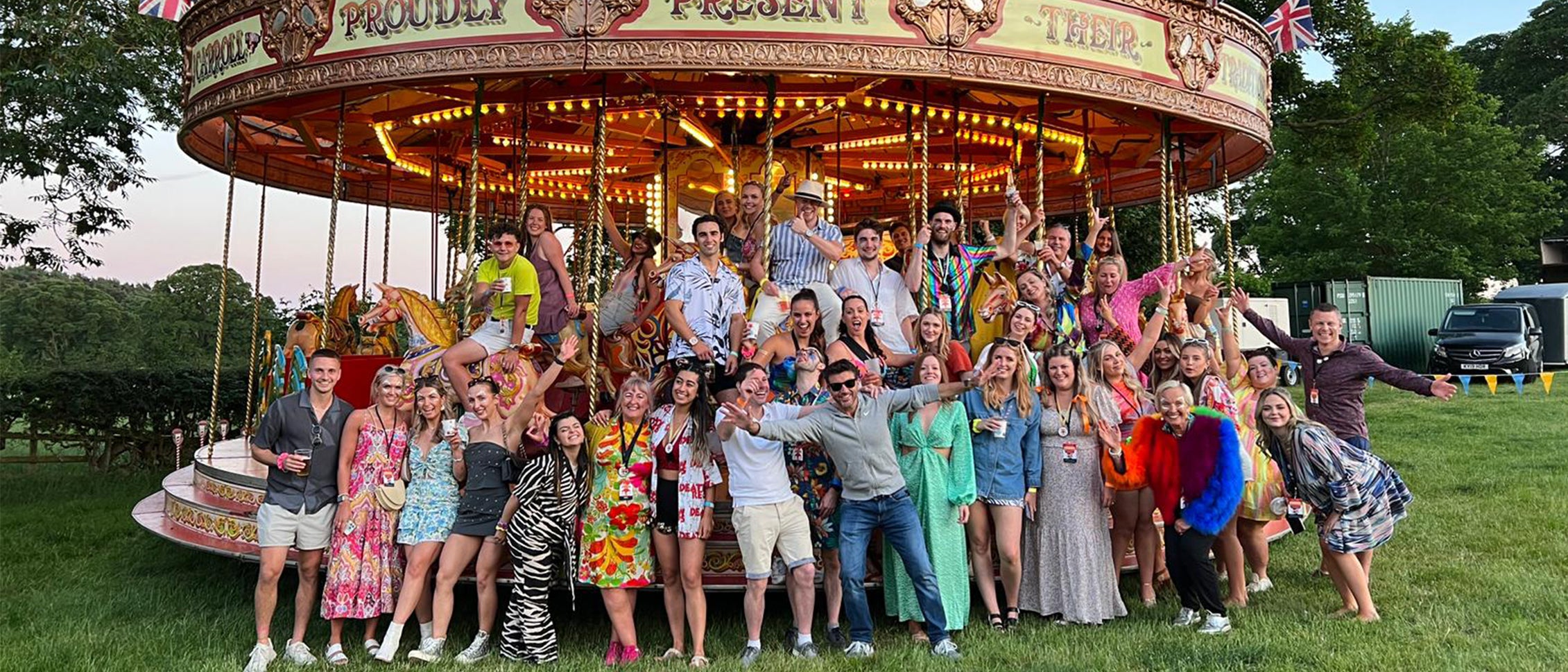 A group of CLOUD NINE employees smiling at a summer party in front of a horse carousel.