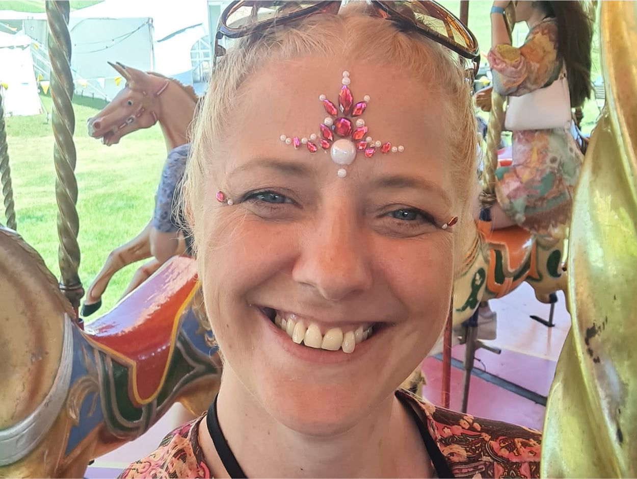 Julie, a CLOUD NINE employee, smiling at the camera with festival gems on her face.