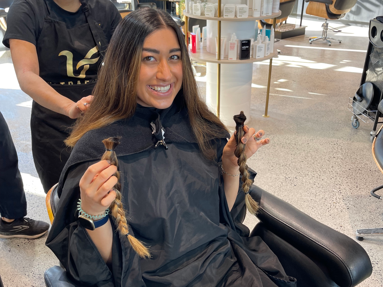 A girl smiling after cutting off her hair for charity. She is sitting in a salon chair and holding the hair in her hands.