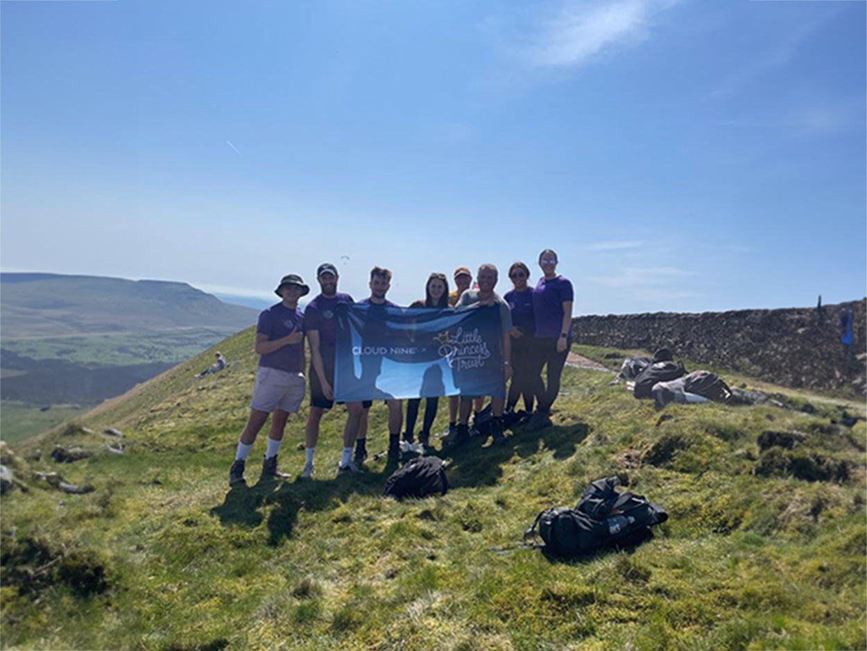 A group on top of a hill holding a flag showcasing the CLOUD NINE x Little Princess Trust collaboration. 