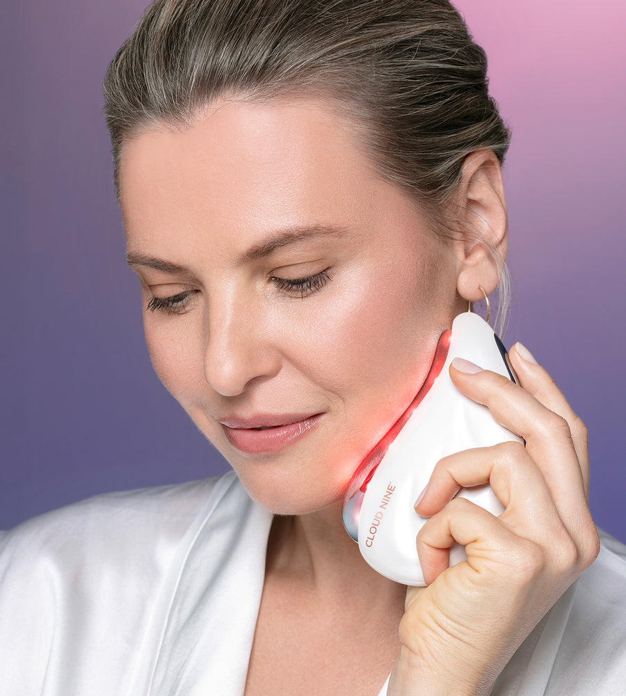 A model using the Redefine Beauty Device across her jawline using red light therapy.