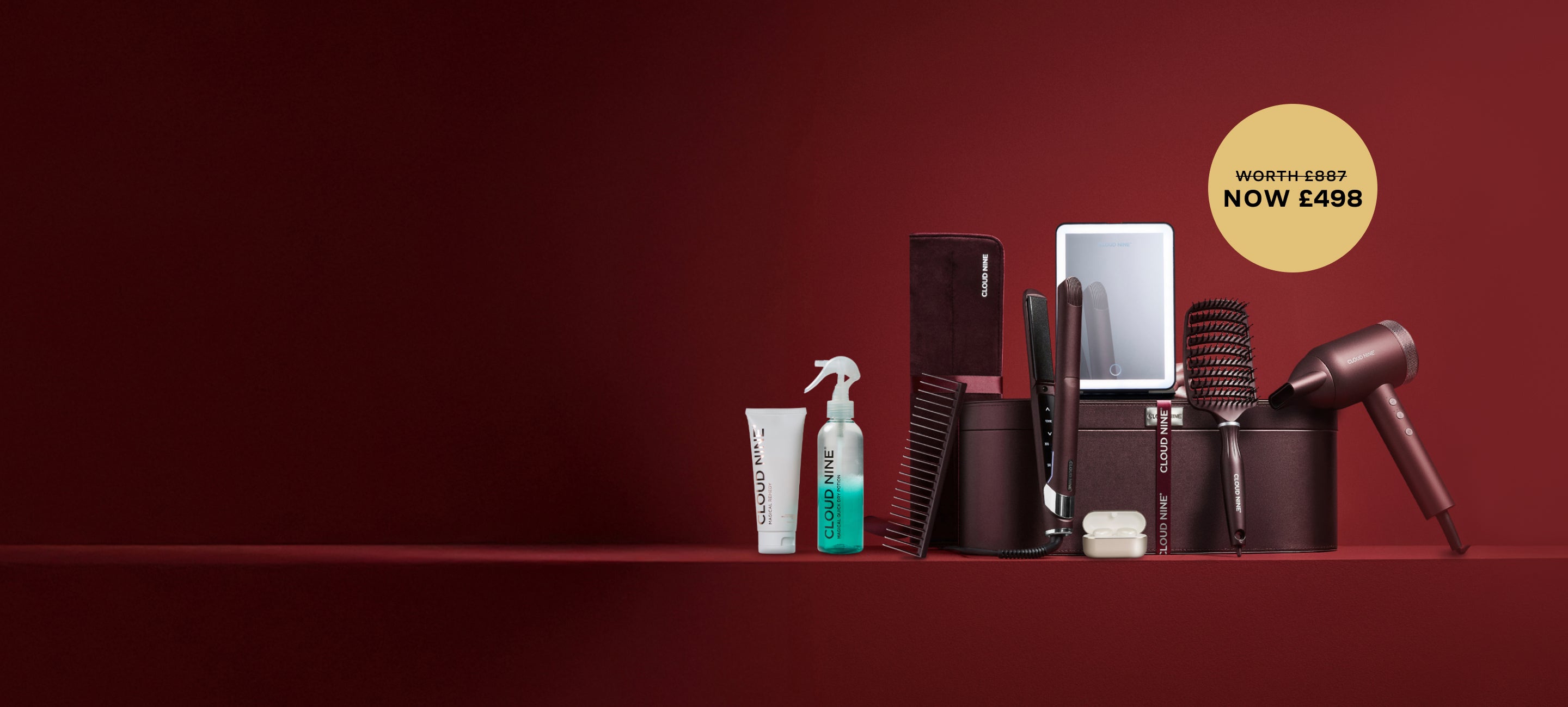 Dark Burgundy set of hair straightener and hair dryer against a leather luxury case. Surrounded by free gifts including a burgundy hair brush and comb, an LED Vanity Mirror, Earbuds and other hair products, with promotional label to show it is worth £887 but is now £498.