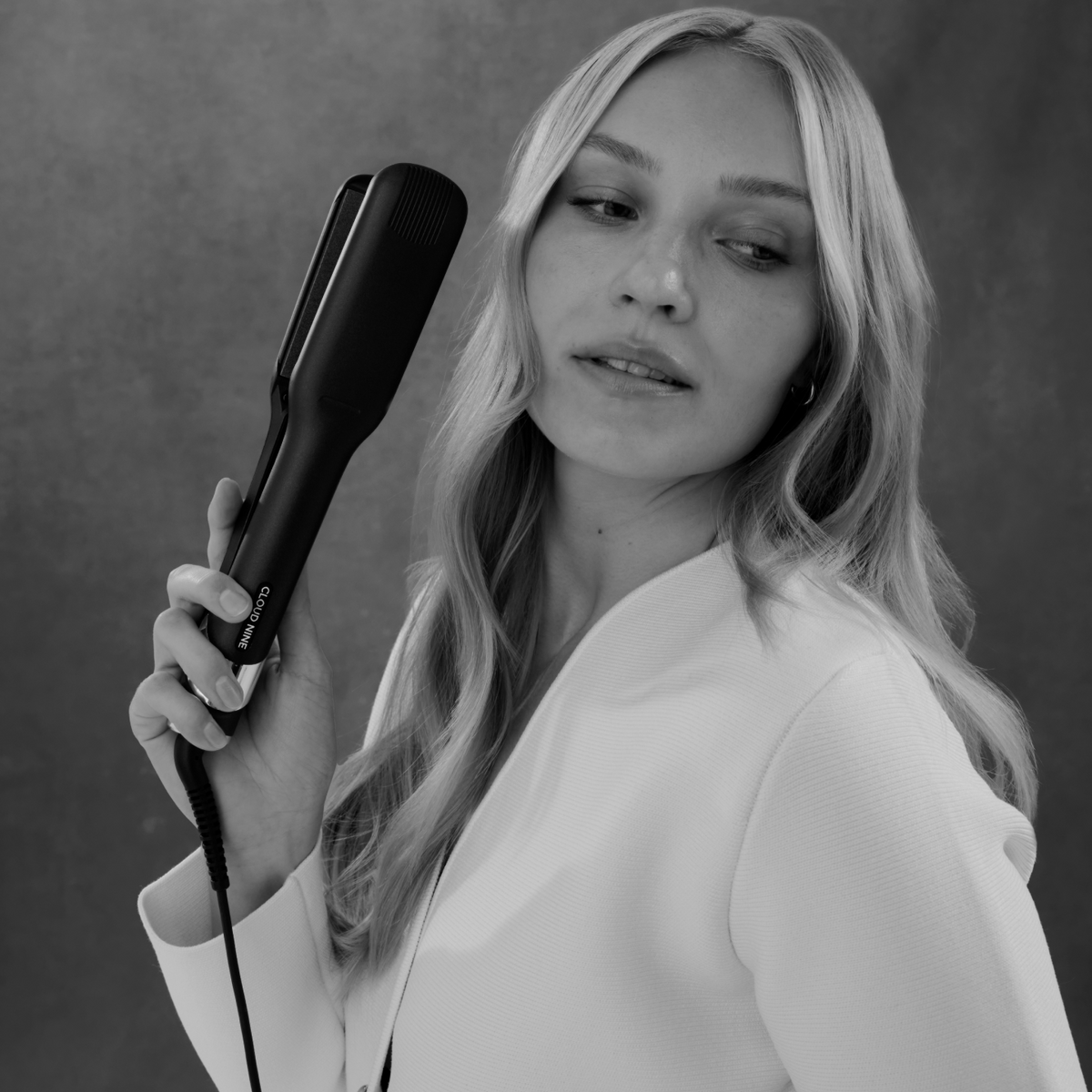 Woman holding a wide hair straightener against a plain background