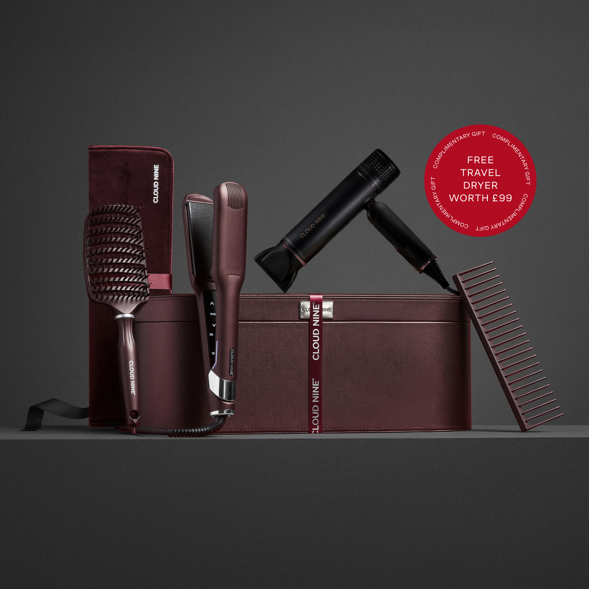 Set of Cloud Nine Dark Burgundy hair styling tools including a brush, comb, straightener, and dryer against a leather luxury case. With a red roundel showing Free Travel Dryer worth £99 offer.