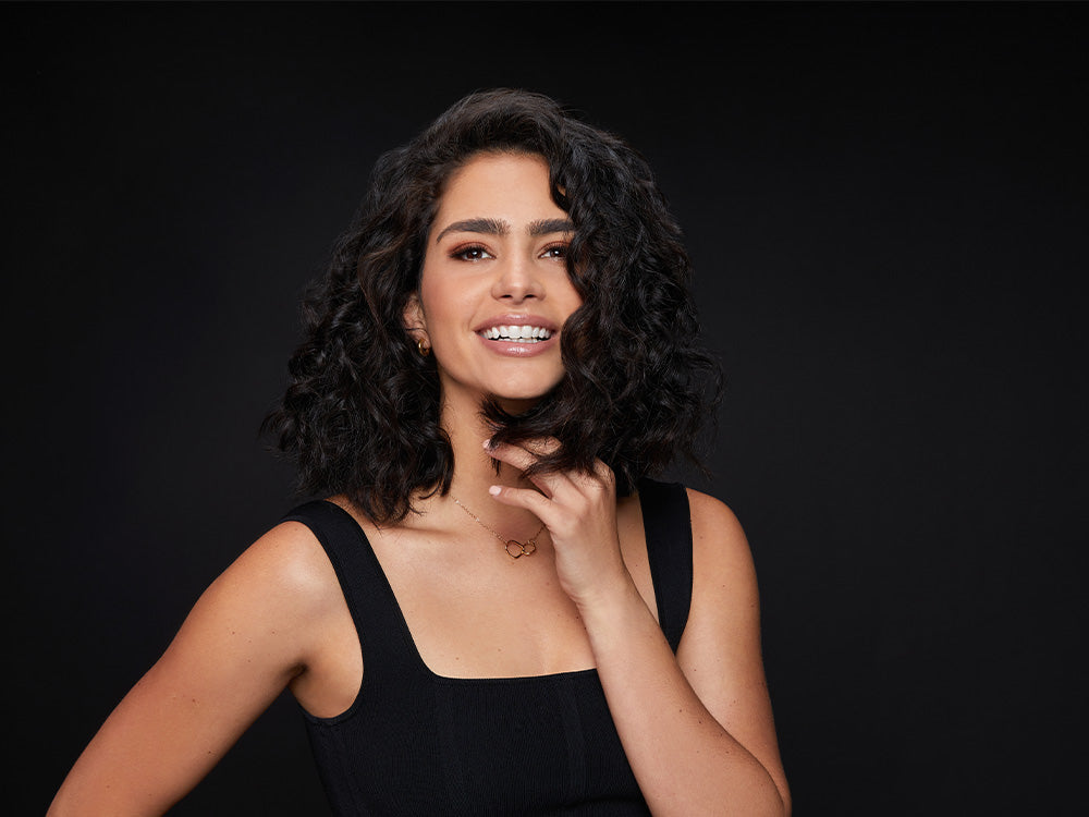 Model with short dark curly hair smiling at the camera.