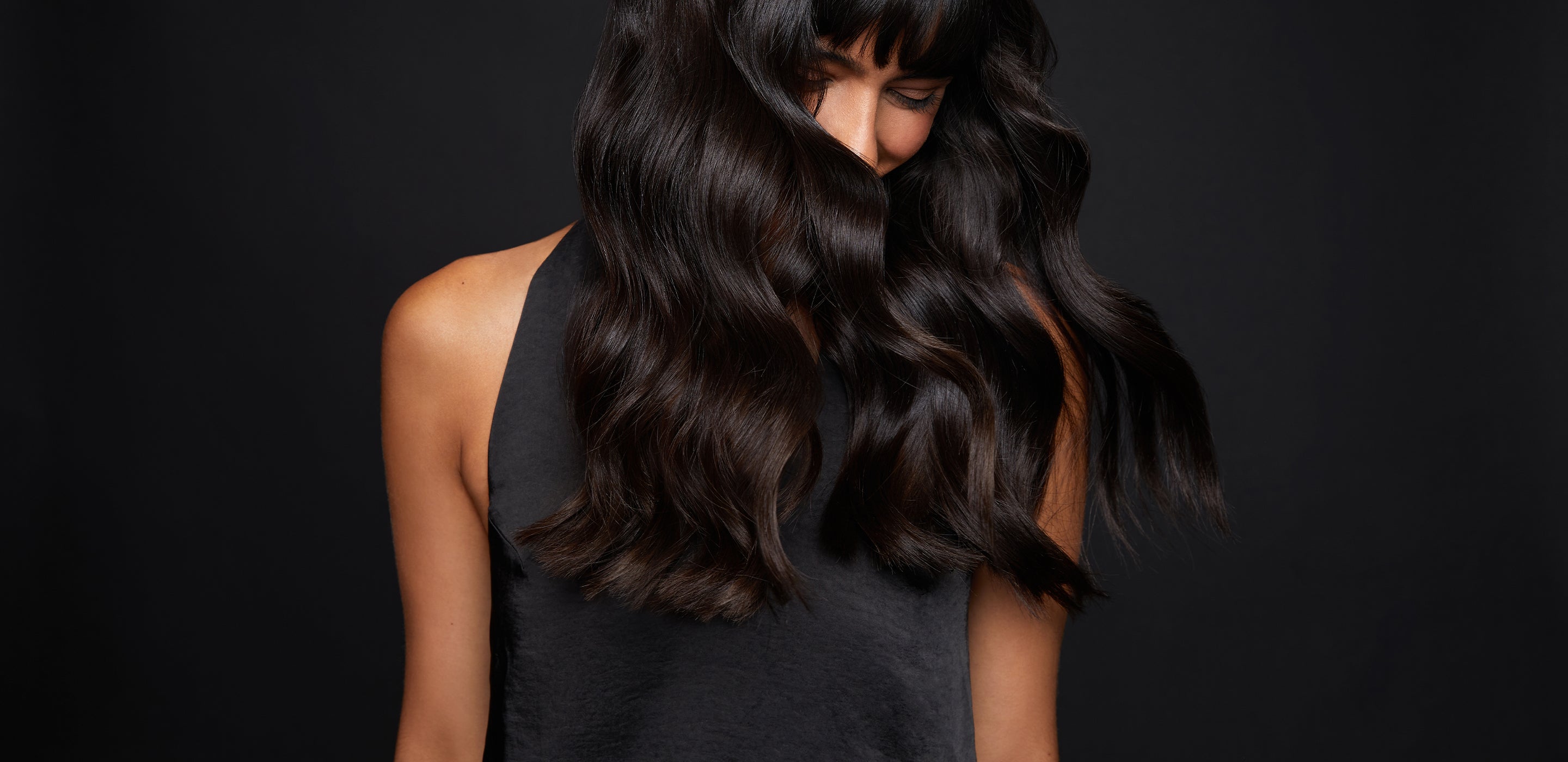 Woman with dark brown wavy hair flowing across her face, on a black background.