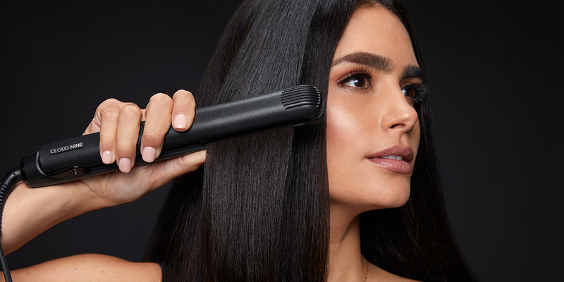 Model looking to right while gliding a black hair straightener through black hair.