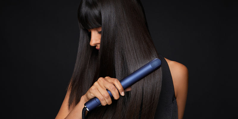 Model looking down as she glides a blue straightener through her black hair.