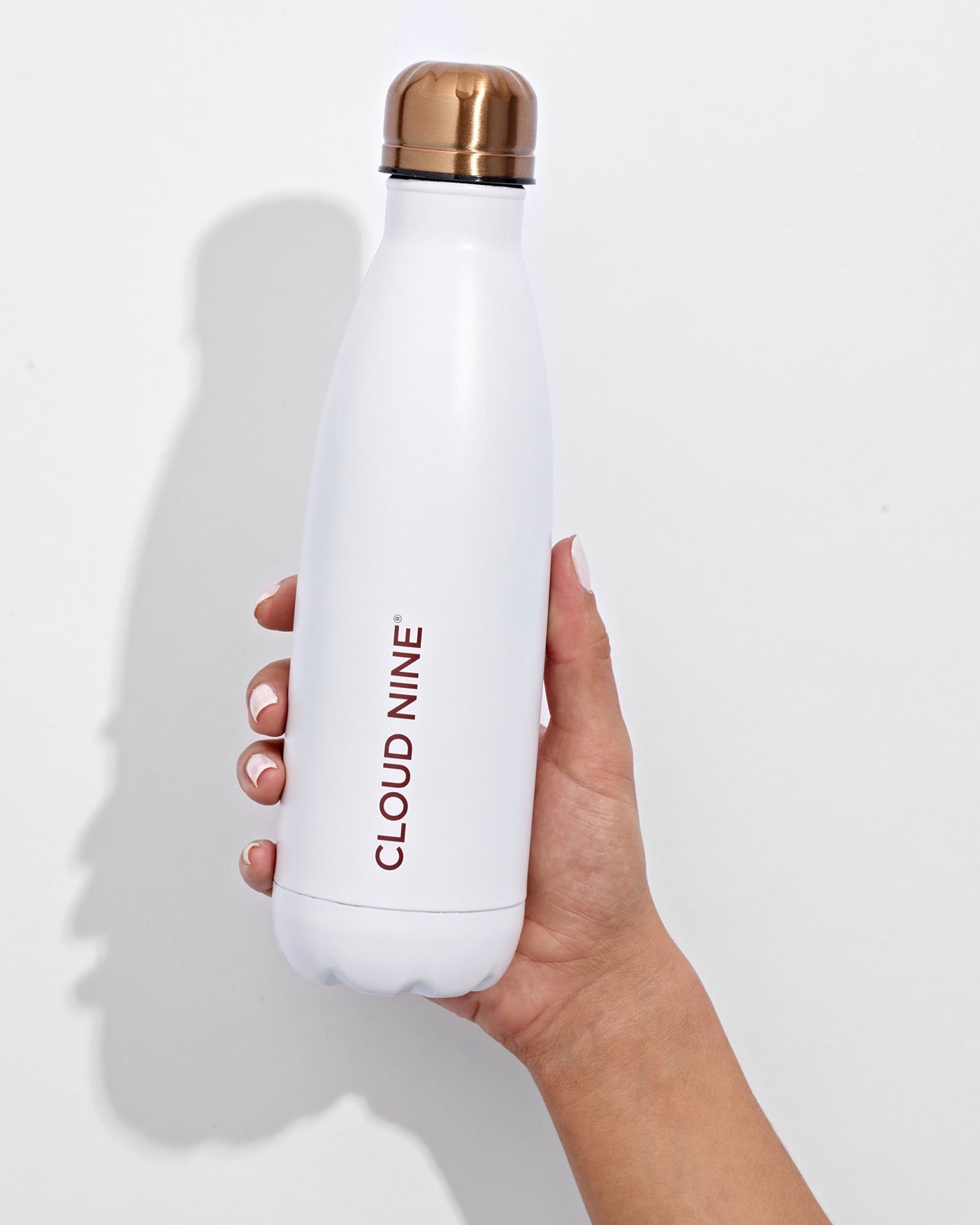A hand holding up a white CLOUD NINE reusable water bottle against a white background.