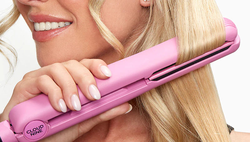 Smiling model running a pink CLOUD NINE hair straightener through blonde hair.
