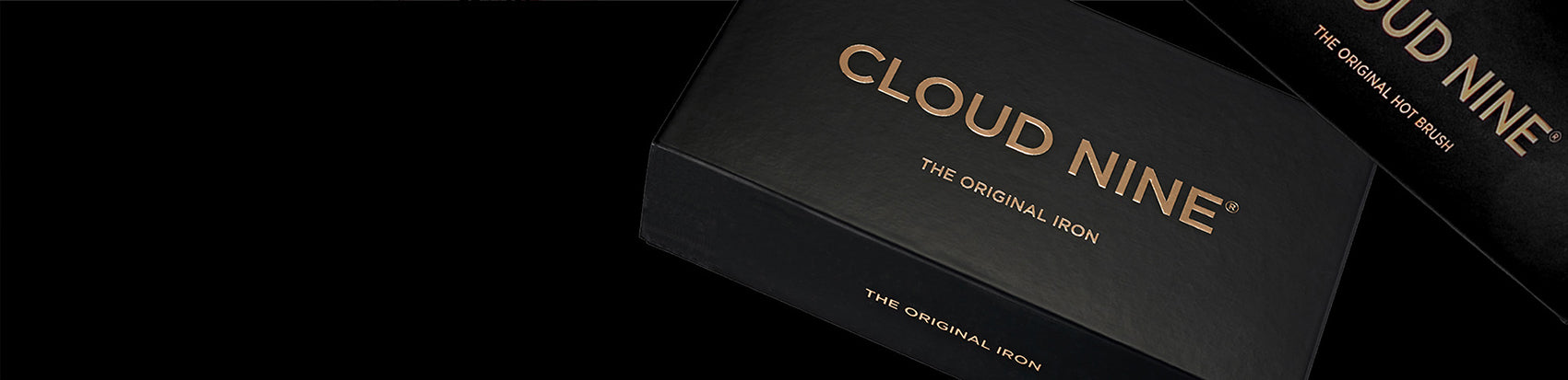 Close up of the CLOUD NINE Original Iron and Hot Brush packaging in black, with a black background. 