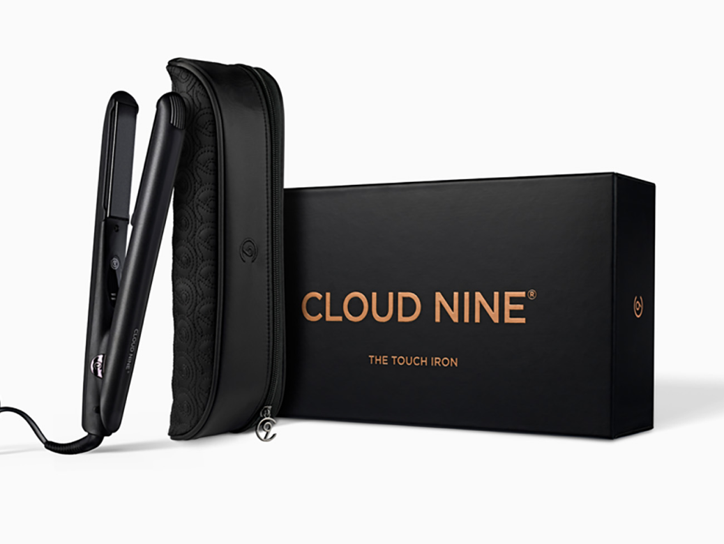 A black CLOUD NINE straightener leaning on a black protective case next to some black packaging for the CLOUD NINE Touch Iron on a white background.