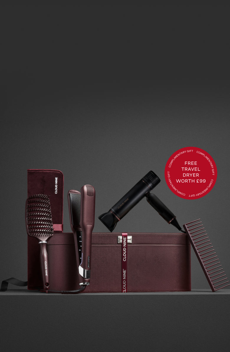Set of Cloud Nine Dark Burgundy hair styling tools including a brush, comb, straightener, and dryer against a leather luxury case. With a red roundel showing Free Travel Dryer worth £99 offer.