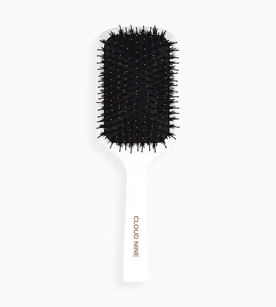 Full view of a CLOUD NINE white paddle brush with black bristles standing upright.