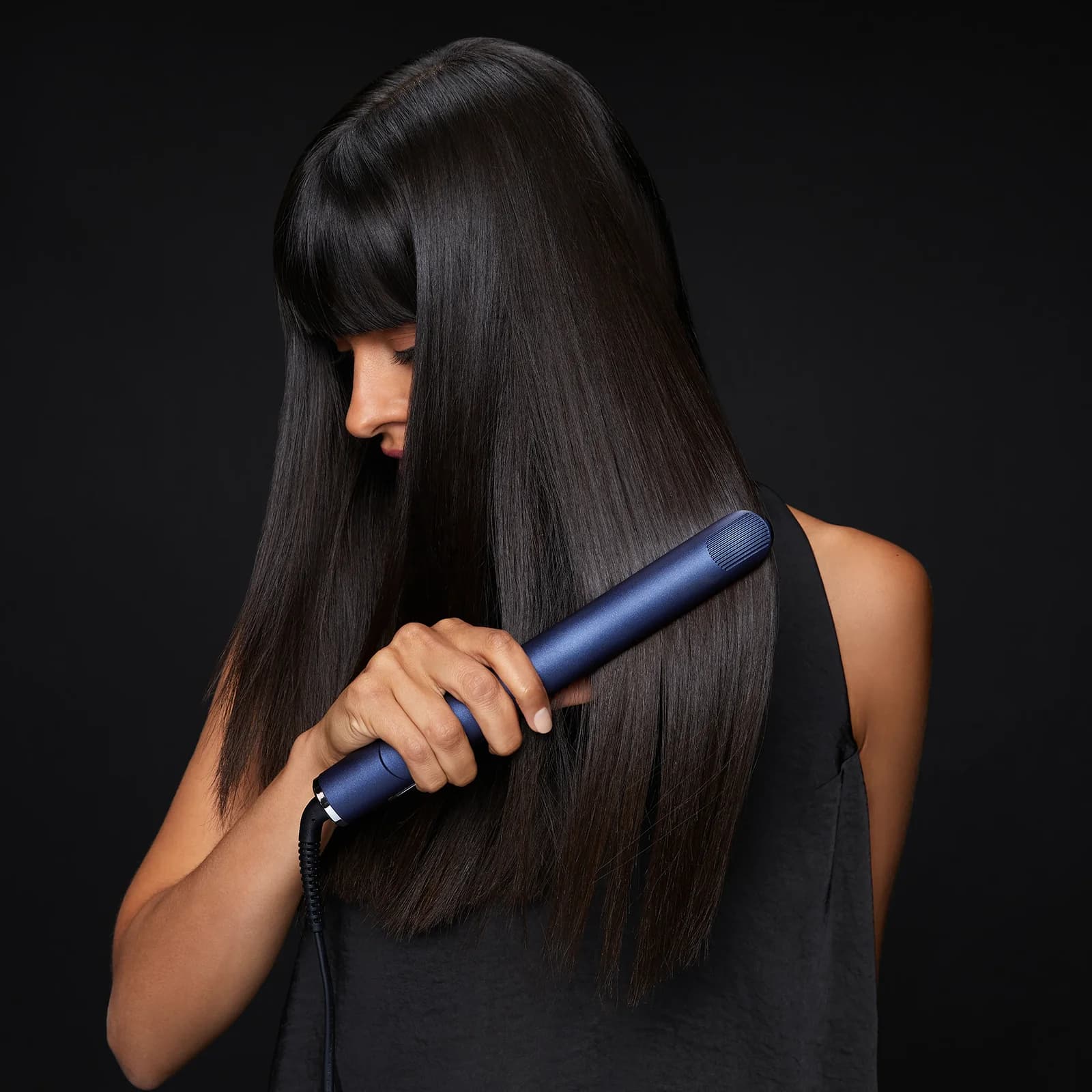 side view of female model with jet black long straight hair holding 2-in-1 Contouring Iron Pro in hand while straighteneing her hair