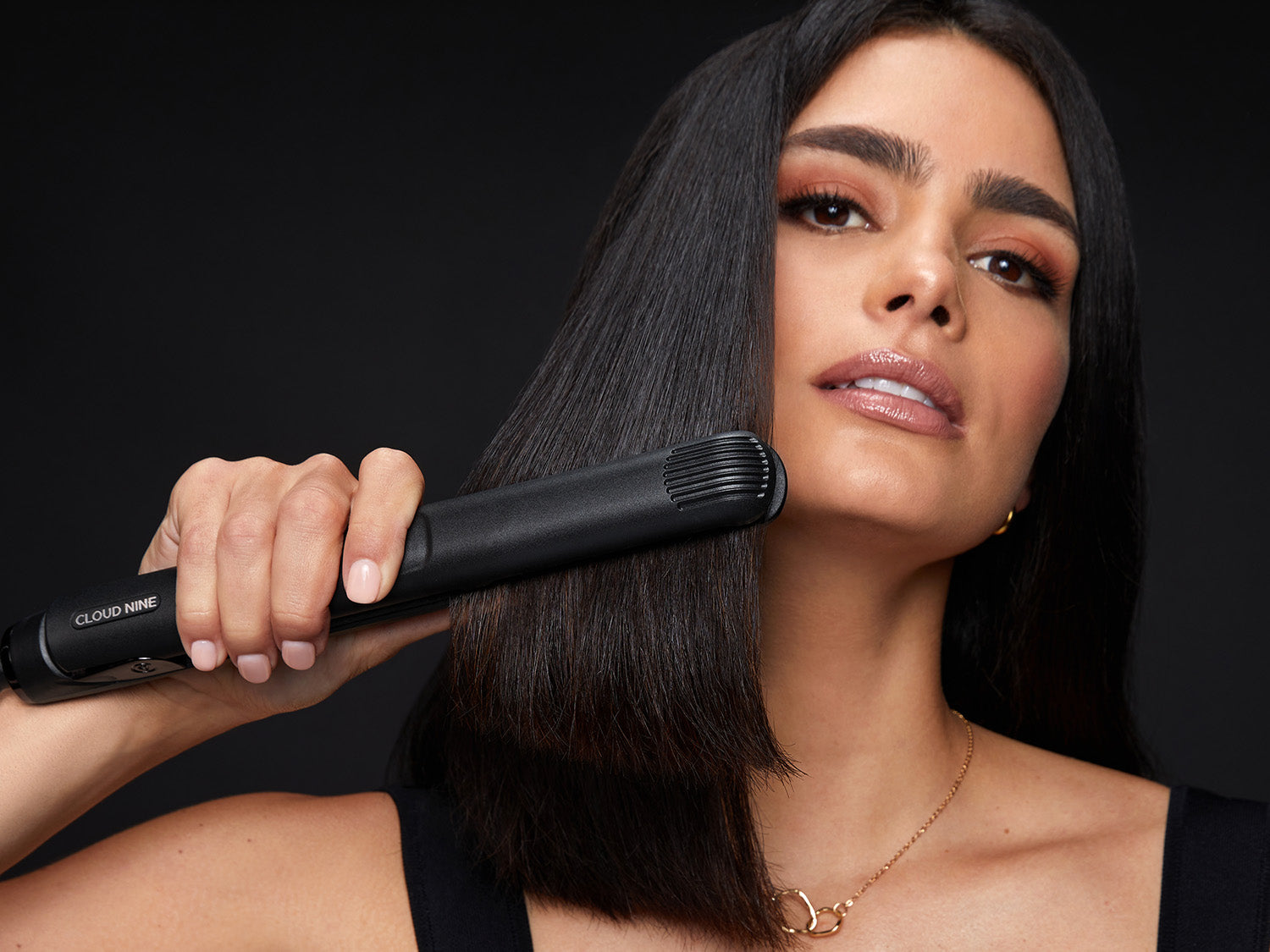 A model with head tilted back holding a black CLOUD NINE straightener through black hair.